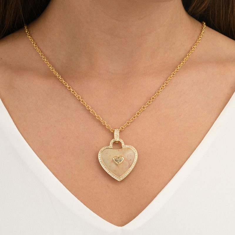 בחורה עונדת תליון לב עשוי אבן הר הבית מוחלקת בצורת לב עם מסגרת יהלומים בזהב צהוב